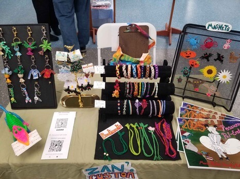 A picture of a table at an arts festival with multiple colorful weavings on displays.